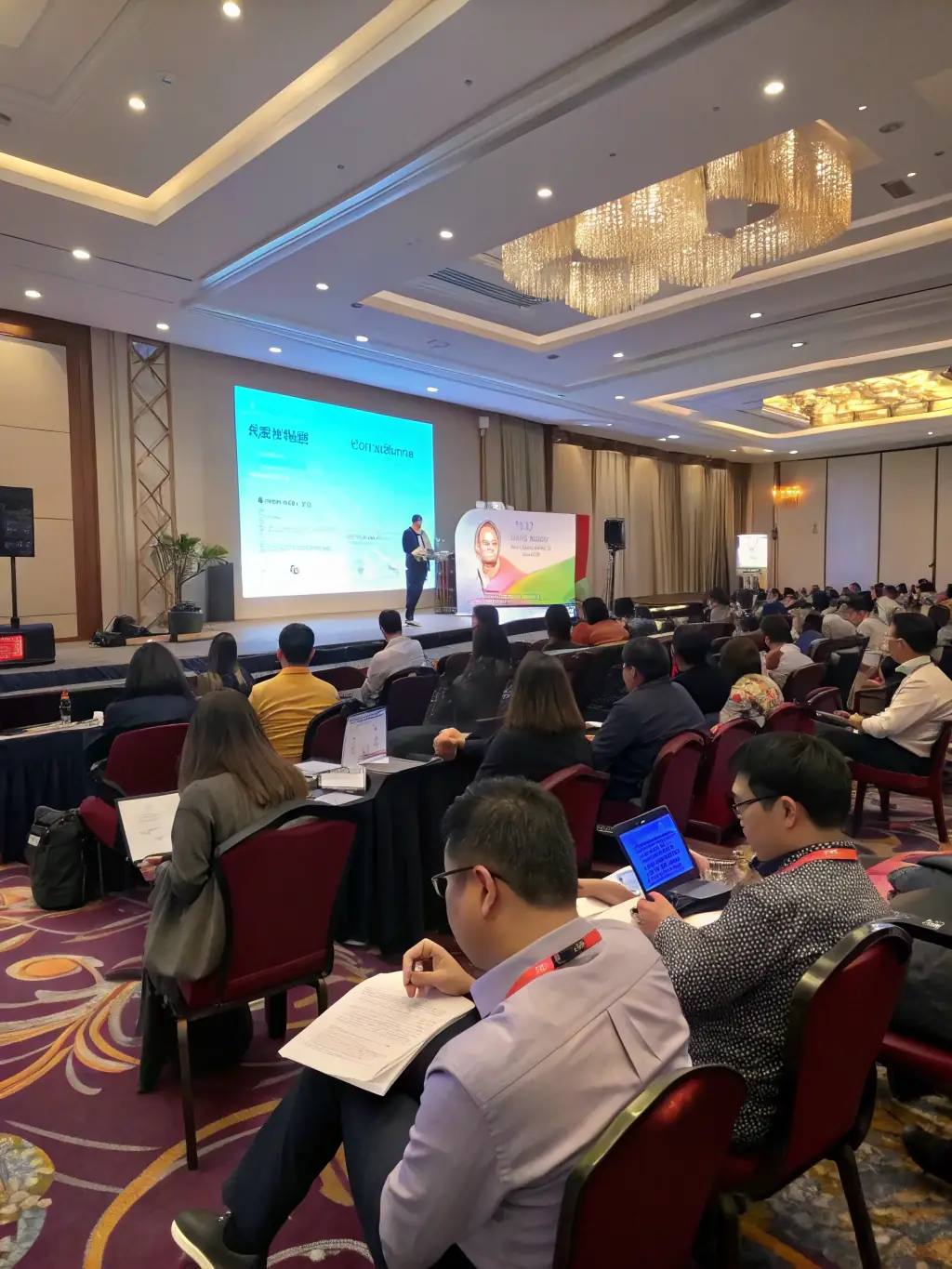 A modern conference hall with attendees listening to a speaker on stage, focusing on risk management strategies.